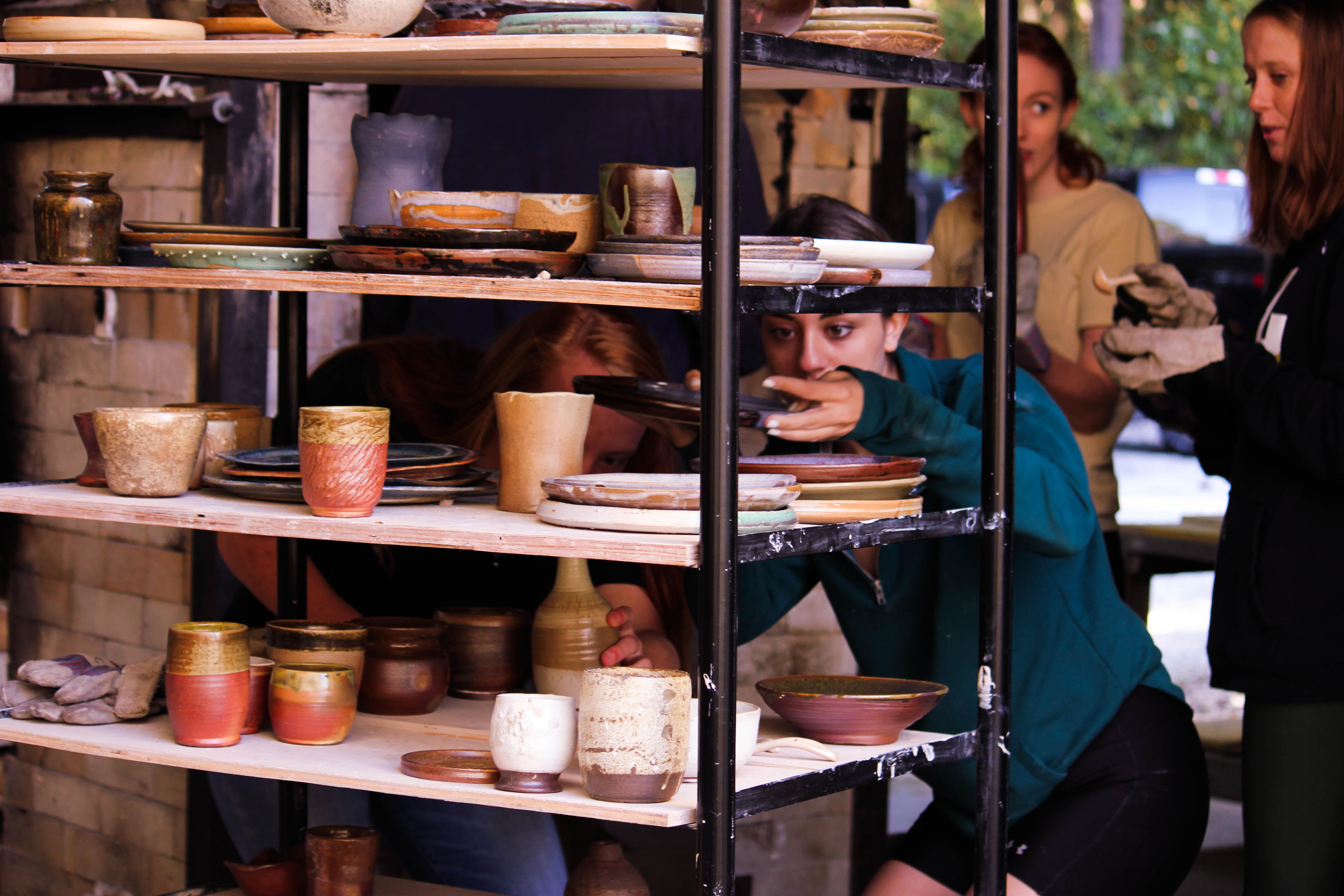 Ceramic students unloading a wood kiln and placing the artwork on transport ware cart shelves.