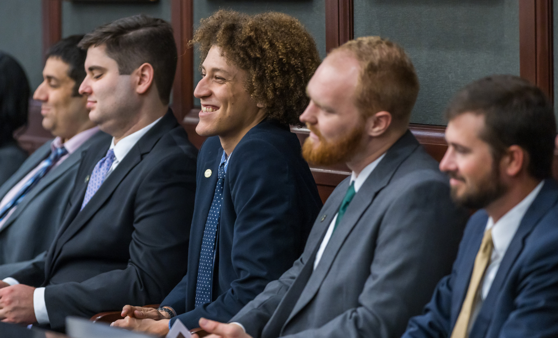 A group of male students sitting in a courtroom jury box, smiling. 