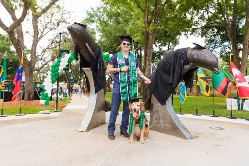 A military veteran standing at the dolphin statue after graduation.